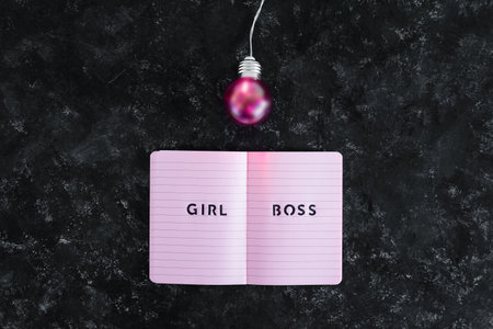 equal opportunities Girl Boss text on top of pink notebook with bright pink light bulb symbol of ideas and inventiveness on black backgroundの写真素材