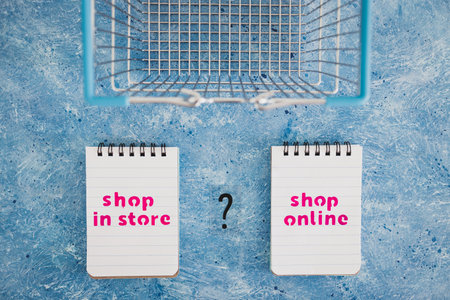 competition and retail industry conceptual image, shop in store vs shop online texts on notepads with shopping basket and question mark symbol of indecisionの写真素材