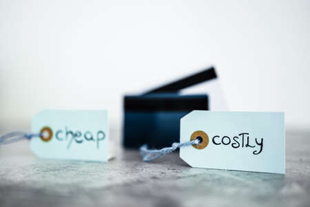 Cheap vs Costly prioduct price tags next to payment cards, money and consumer behaviour conceptual imageの写真素材