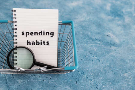spending habits text on notepad with shopping basket and magnifying glass, money and consumer behaviour conceptual imageの写真素材