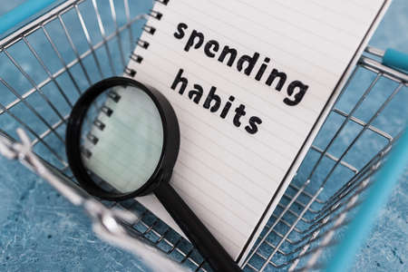 spending habits text on notepad with shopping basket and magnifying glass, money and consumer behaviour conceptual imageの写真素材