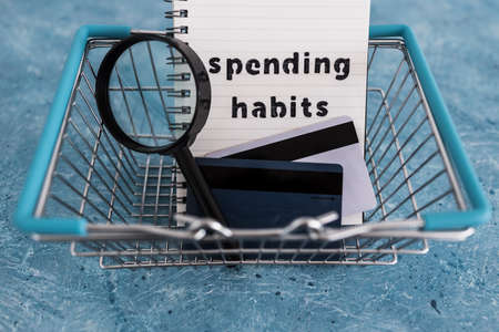spending habits text on notepad with shopping basket and magnifying glass and payment cards, money...