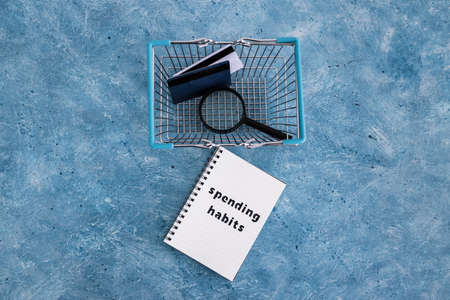 spending habits text on notepad with shopping basket and magnifying glass and payment cards, money and consumer behaviour conceptual imageの写真素材
