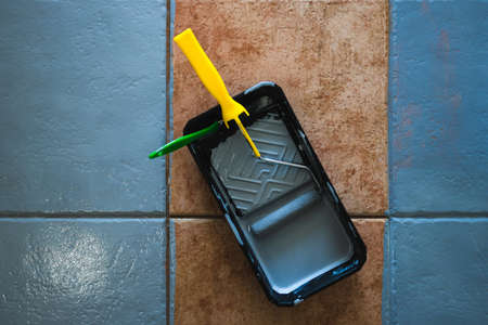 paint roller with brush and tray next to open pot of paint shot from above surrounded by terracotta floor tiles being painted gray, diy and home renovation conceptの写真素材