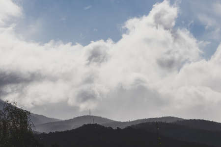 contrasty sky with thick clouds and intense sunlight peeking through them, shot in Tasmania Australia with mountains in the backgroundの写真素材