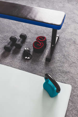 home gym with mixed fitness items including yoga mat abs bench weights and skipping rope with subtle grey and blue tonesの写真素材