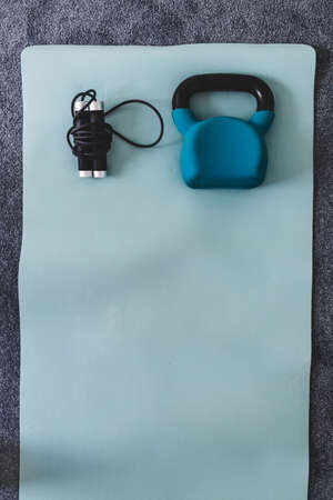 kettlebell and skipping rope on yoga mat indoor, concept of home gym and weight training vs cardio fitness styled with subtle grey and blue tonesの写真素材