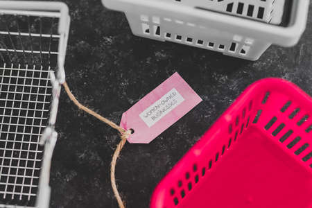 women-owned businesses tag with pink shopping basket among other competitor ones on black background, supporting equality and equal opportunitiesの写真素材