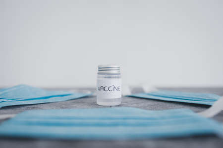 vaccine ampoule surrounded by surgical face masks, vaccine race and immunisation against the pandemicの写真素材