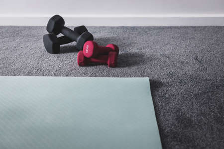 home gym with mixed fitness items including yoga mat and different sets of dumbbells on the floor