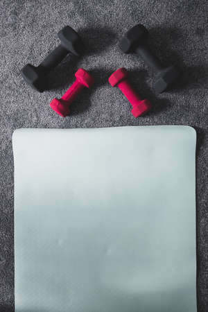 home gym with mixed fitness items including yoga mat and different sets of dumbbells on the floorの写真素材