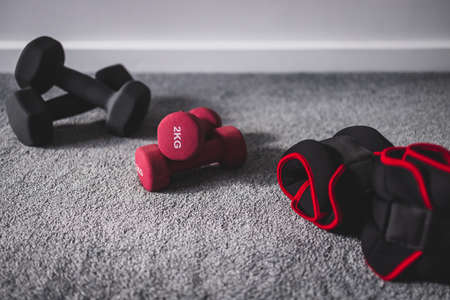 home gym with mixed fitness items including ankle weights and different sets of dumbbells on the floorの写真素材
