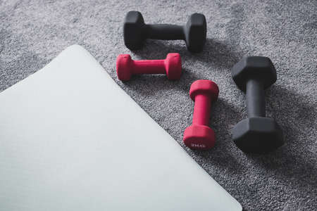 home gym with mixed fitness items including yoga mat and different sets of dumbbells on the floorの写真素材