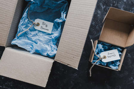 product tags with small business vs big brand texts inside of bigger and smaller delivery parcels, concept of customer behaviour and supporting small local businessesの写真素材