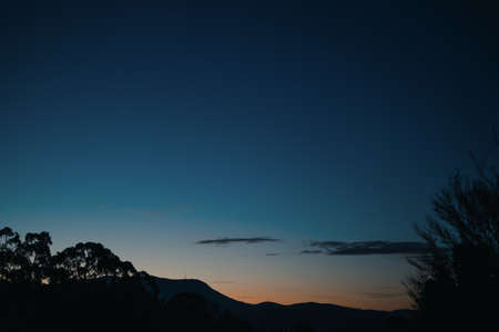 sunrise with clouds rolling over the mountains and thick vegetation shot in Tasmania, Australia in...