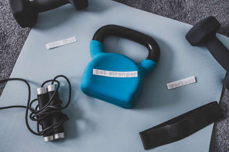 Gym time and exercising in your spare time conceptual image, kettlebell with dumbbells and skipping rop on yoga mat on bedroom floor with Get Stronger messageの写真素材