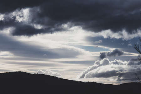 thick stormy clouds over the mountains with intense sunlight peaking through and contrasty tones shot in Tasmania, Australia in winterの写真素材