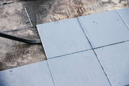 blue outdoor tiles getting ripped up to reveal concrete paving underneath, concept of demolition or...