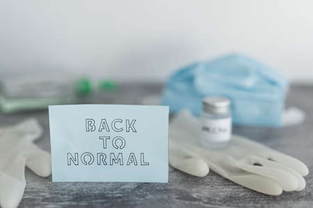 covid-19 vaccine race and life after the pandemic, Back to Normal message with Vaccine ampoule next to disposable gloves, hand sanitizer and face mask in the backgroundの写真素材