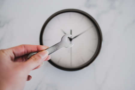 hand holding wrench in front of big clock shot at shallow depth of field, metaphor of productivity and time managementの写真素材