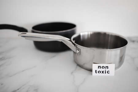 healthy cooking and harsh chemicals concept, stainless steel vs non stick saucepan side by side with...