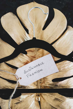 Sustainable Fashion label with clothes hanger on top of golden leaf on black background shot at...