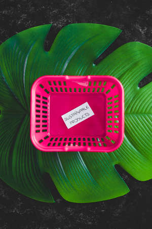 buying sustainable products concept of ecoogy and consumer behaviour, empty pink shopping basket with text on top of tropical green leafの写真素材