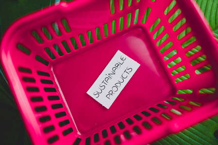buying sustainable products concept of ecoogy and consumer behaviour, empty pink shopping basket with text on top of tropical green leafの写真素材
