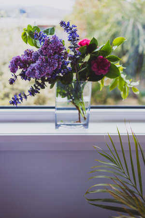close-up of bunch of purple flowers including lillac in vase indoor by the window shot at shallow depth of fieldの写真素材