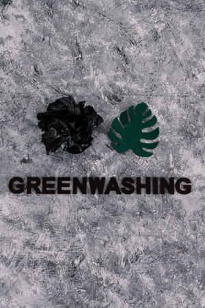 greenwashing and companies pretending to be sustainable conceptual image, paper leaf next to piece of waste with text underneathの写真素材