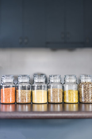 clear pantry jars with different types of grains and legumes including quinoa  lentils buckwheat and barley on benchtop with kitchen bokeh, simple ingredients conceptの写真素材