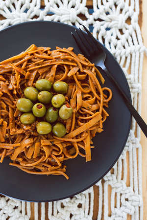 vegan red pesto spaghetti and fettuccini mix with green olives topping, healthy plant-based food recipesの写真素材