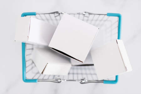 shopping and add to cart concept, parcels of different shapes piled up inside of shopping basket on light marble background shot at shallow depth of fieldの写真素材