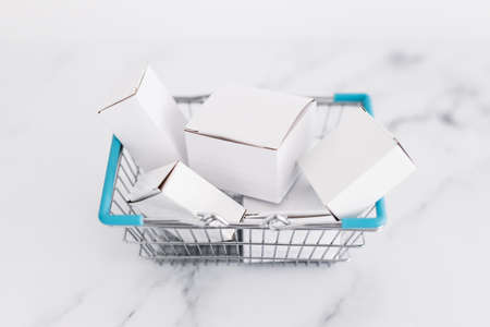 shopping and add to cart concept, parcels of different shapes piled up inside of shopping basket on light marble background shot at shallow depth of fieldの写真素材
