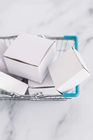 shopping and add to cart concept, parcels of different shapes piled up inside of shopping basket on light marble background shot at shallow depth of fieldの写真素材