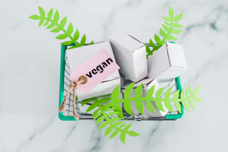 sustainability and cruelty free product concept, shopping basket with blank product packagings and green leaves with Vegan label on themの写真素材