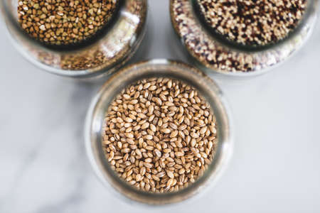 healthy whole grains and legumes in clear pantry jars on marble background including quinoa buckwheat and barley, simple vegan pantry ingredients conceptの写真素材