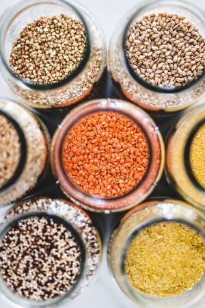 red lentils and other healthy whole grains and legumes in clear pantry jars on marble background, simple vegan pantry ingredients conceptの写真素材