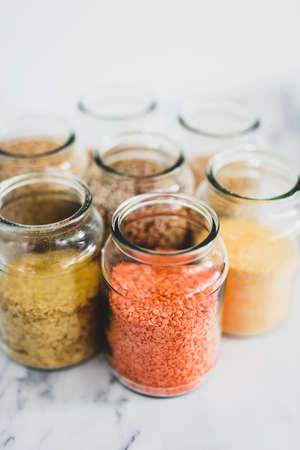healthy whole grains and legumes in clear pantry jars on marble background including quinoa rice buckwheat lentils and barley, simple vegan pantry ingredients conceptの写真素材