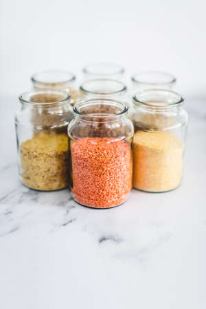 healthy whole grains and legumes in clear pantry jars on marble background including quinoa rice buckwheat lentils and barley, simple vegan pantry ingredients conceptの写真素材