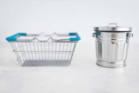 consumerism vs sustainable products and intentional shopping conceptual image, shopping basket for good to be purchased next to recycling bin for excess goods being produced or boughtの写真素材