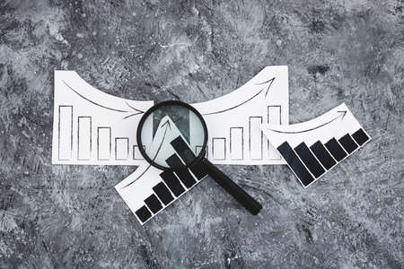 financial markets or money and investments conceptual image, magnifying glass with charts showing upward and downward trendsの写真素材