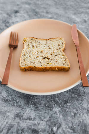 wholegrain multiseeds slice of bread on dining plate with fork and knife, concept of dieting vs healthy nutrition and intuitive eatingの写真素材