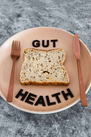gut health text with wholegrain multiseeds slice of bread on dining plate with fork and knife, healthy nutrition and scientific research about the microbiomeの写真素材