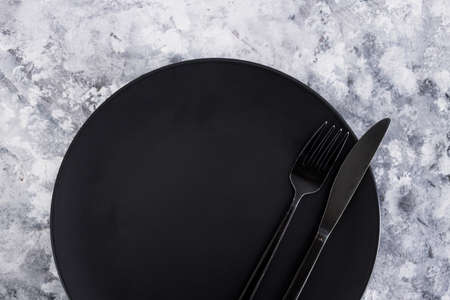 black dining plate with fork and knife on gray background with minimalist composition, concept of dieting vs intuitive eatingの写真素材