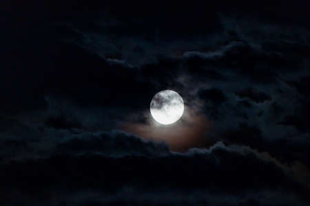 full moon with dark clouds in front of it in the night sky shot with telephoto lens