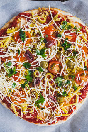 vegan homemade pizza with cherry tomatoes olives and fresh herbs topped with dairy-free cheese, healthy plant-based food recipesの写真素材