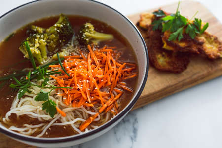 vegan noodles soup with carrots and broccoli with a side of fried bread crumbed zucchini slices, healthy plant-based food recipesの写真素材