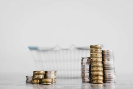 stacks of different coins inside of shopping basket on white background shot at shallow depth of field with minimalist composition, concept of expenses and consumer behaviourの写真素材