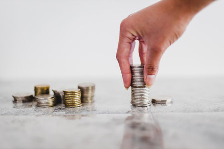 hand placing stacks of different coins on white background shot at shallow depth of field with minimalist composition, including golden and silver onesの写真素材